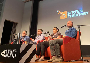 People sitting on a stage with microphones and looking to an audience.